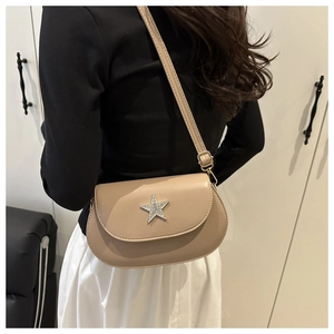 Close-up of beige saddle bag with a large rhinestone star buckle on a shoulder strap