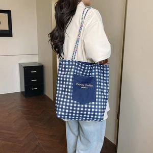 Blue and white plaid canvas tote bag with a dark blue outer pocket and woven straps