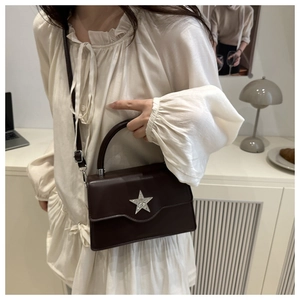 Sac bandoulière marron avec étoile argentée et bandoulière sur une chemise blanche