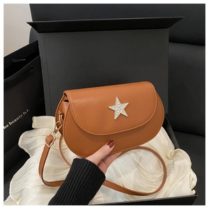 Brown saddle crossbody bag with rhinestone star detail inside a luxury black gift box