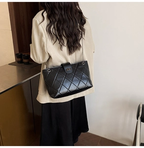 Detail of black quilted shoulder bag featuring glossy finish and dark metal chain strap