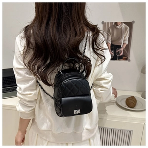 Detail view of a black quilted mini backpack with chain straps on a model's back