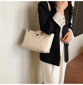 Detail of quilted beige tote bag with chain strap and metallic twist lock closure