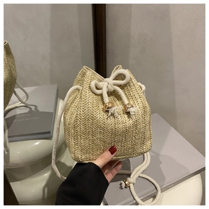 Detailed close-up of straw bucket bag with herringbone weave and gold ball drawstring