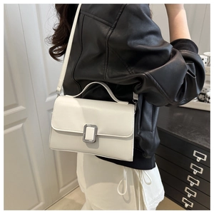 Gros plan d'un sac à bandoulière en cuir blanc avec boucle argentée porté par un mannequin