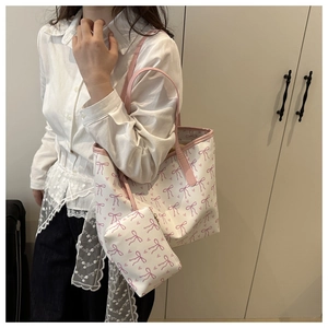 Side view of a white tote bag with pink bow patterns and a small matching purse charm