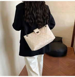 Detail of a beige quilted crossbody bag with a metal twist lock and chain strap