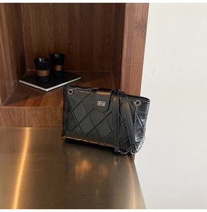 Detail of black quilted chain shoulder bag featuring a silver metal twist lock closure