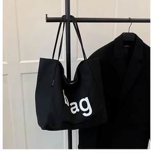 Close-up of black canvas tote bag with white bag lettering and fashion side label