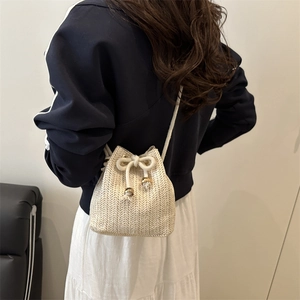 Minimalist beige woven straw bucket bag with gold accents shown on a female model