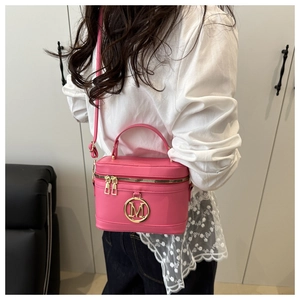 Pink box crossbody bag with gold M logo shown on model with casual white shirt