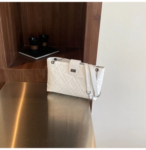 Detail of white quilted handbag with silver twist lock and metal chain strap texture