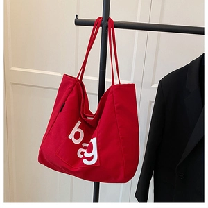 Detail of red canvas tote bag featuring white BAG letter print and sturdy shoulder straps