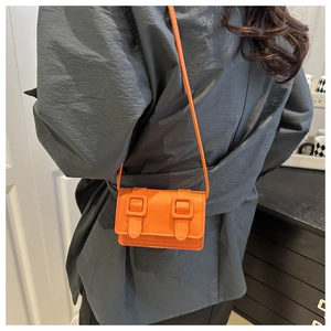 Detail of mini orange crossbody bag with double square buckles on model