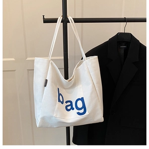 Detail of white canvas tote bag with blue bag print and fashion label on shoulder strap