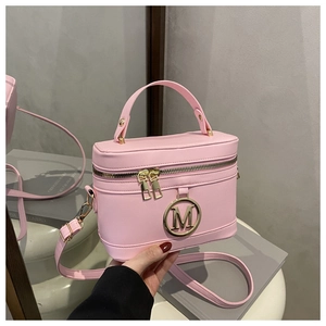 Detail of pink vanity bag with gold M logo held by model against a minimalist background