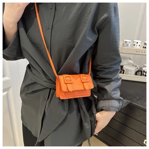 Mini orange crossbody bag with knit buckle detail shown on model with dark shirt