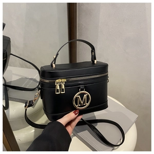 Detail of vintage black vanity bag featuring a gold metal M logo and smooth leather texture