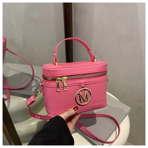 Detail of pink box crossbody bag with gold M logo, dual zippers, and top handle