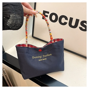 Detail of navy canvas tote with colorful woven handles and embroidered gold logo