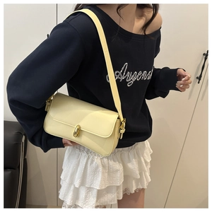 Detail of light yellow leather shoulder bag with gold oval twist lock on a model