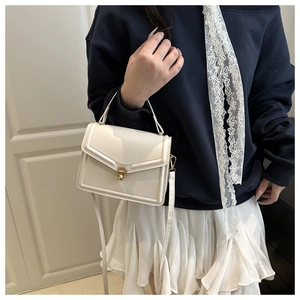 Detail of cream white crossbody bag with gold ring clasp worn by model in casual style