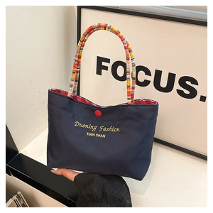 Detail of navy blue tote bag with multi-color braided handles and red metal clasp