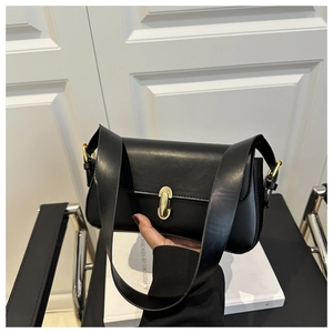 Detail of black leather shoulder bag with gold oval clasp and sleek wide strap design