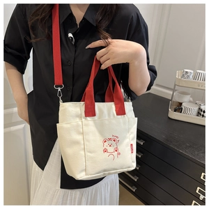 Dettaglio dei manici rossi e della tracolla regolabile della borsa tote color crema