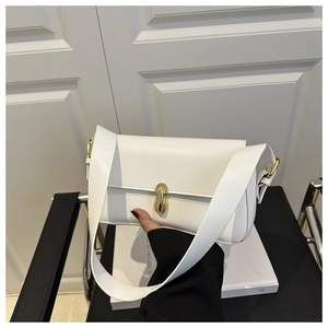 Close-up of minimalist white leather shoulder bag with oval gold buckle and wide strap