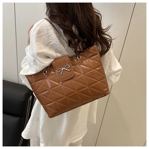 Detail of brown quilted tote bag with silver bow clasp and woven chain strap