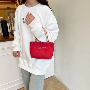 Red stylish handbag with colorful beaded handle and golden logo in a modern cafe setting