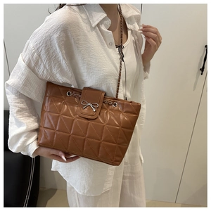 Detail of brown quilted underarm bag with silver bow ornament and chain strap