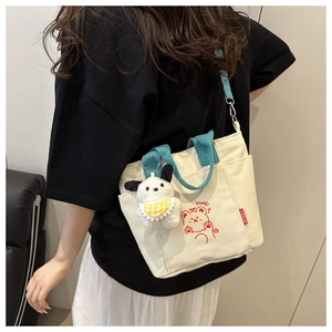 Detail view of cream canvas bag with blue straps and plush dog charm accessory