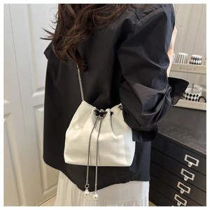 Detail of white crocodile pattern bucket bag featuring a butterfly buckle and pearl tassels