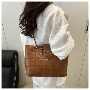Detail of brown quilted tote bag with silver bow ornament and chain strap