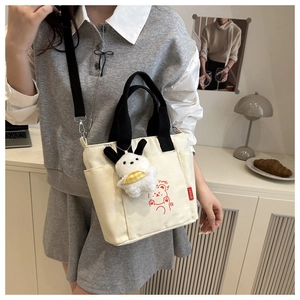 Dettaglio della borsa tote in tela beige con stampa orsetto e ciondolo in peluche sul modello