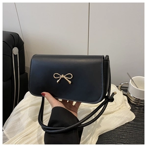 Close-up of black crossbody bag featuring a golden metal bow and matte finish