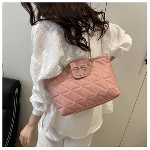 Close-up of pink quilted tote bag with silver bow accent and chain strap worn by a model