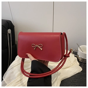 Detail of red leather crossbody bag with a golden bow buckle on white textured cloth