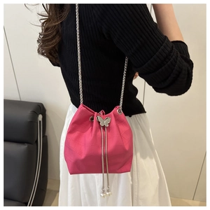 Detail of fuchsia leather bucket bag with silver butterfly charm and pearl tassel strap
