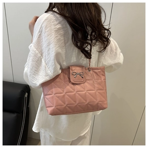 Close-up of pink quilted tote bag with silver bow charm worn by a model in a minimal room