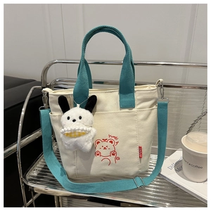 Dettaglio borsa tote in tela beige con manici verdi, stampa orso e ciondolo con coniglio