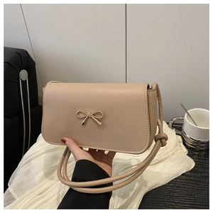Detail of beige square handbag featuring a golden bow ornament and knotted shoulder strap