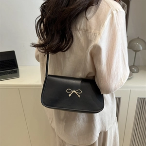 Sac baguette noir minimaliste avec boucle dorée en nœud, présenté dans un cadre chic