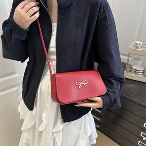 Minimalist red leather crossbody bag featuring a golden metal bow and a flap design