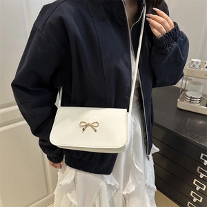 Chic beige crossbody square bag featuring a gold bow detail on a stylish model