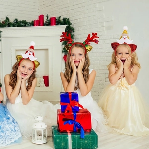 Three children wearing sequined Christmas antler and Santa headbands in a cozy holiday room