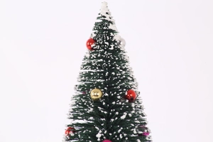 Detail of mini flocked Christmas tree with colorful baubles on white background