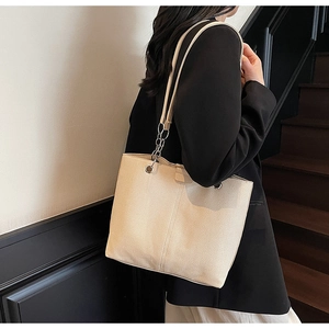 Detail of a large beige canvas tote bag with silver chain strap on a model shoulder